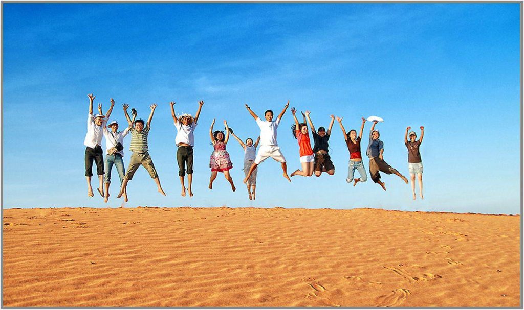 Group of travelers jumping on sand dunes under a blue sky 